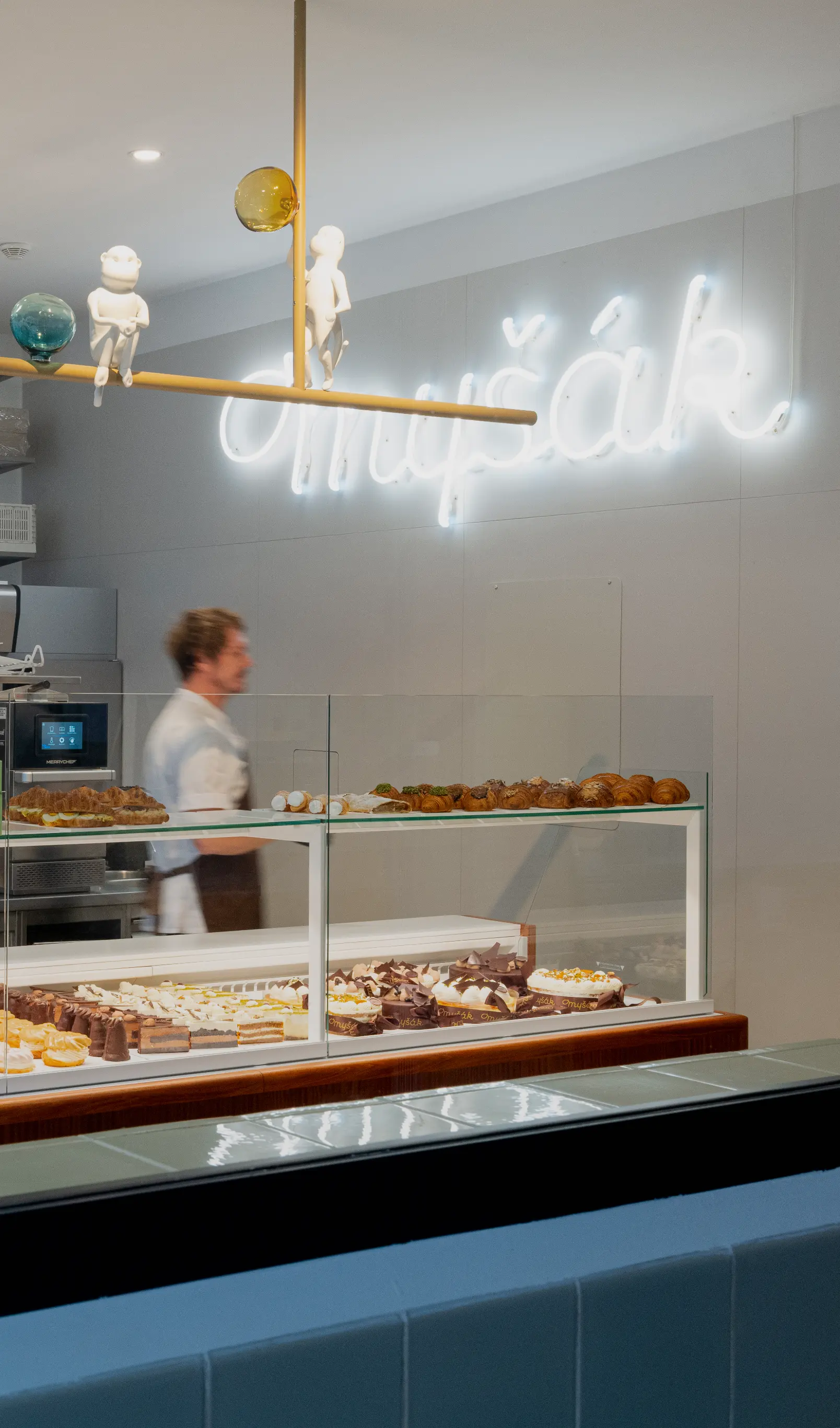 Interiér cukrárny Myšák s obsluhou a vitrínou dezertů.