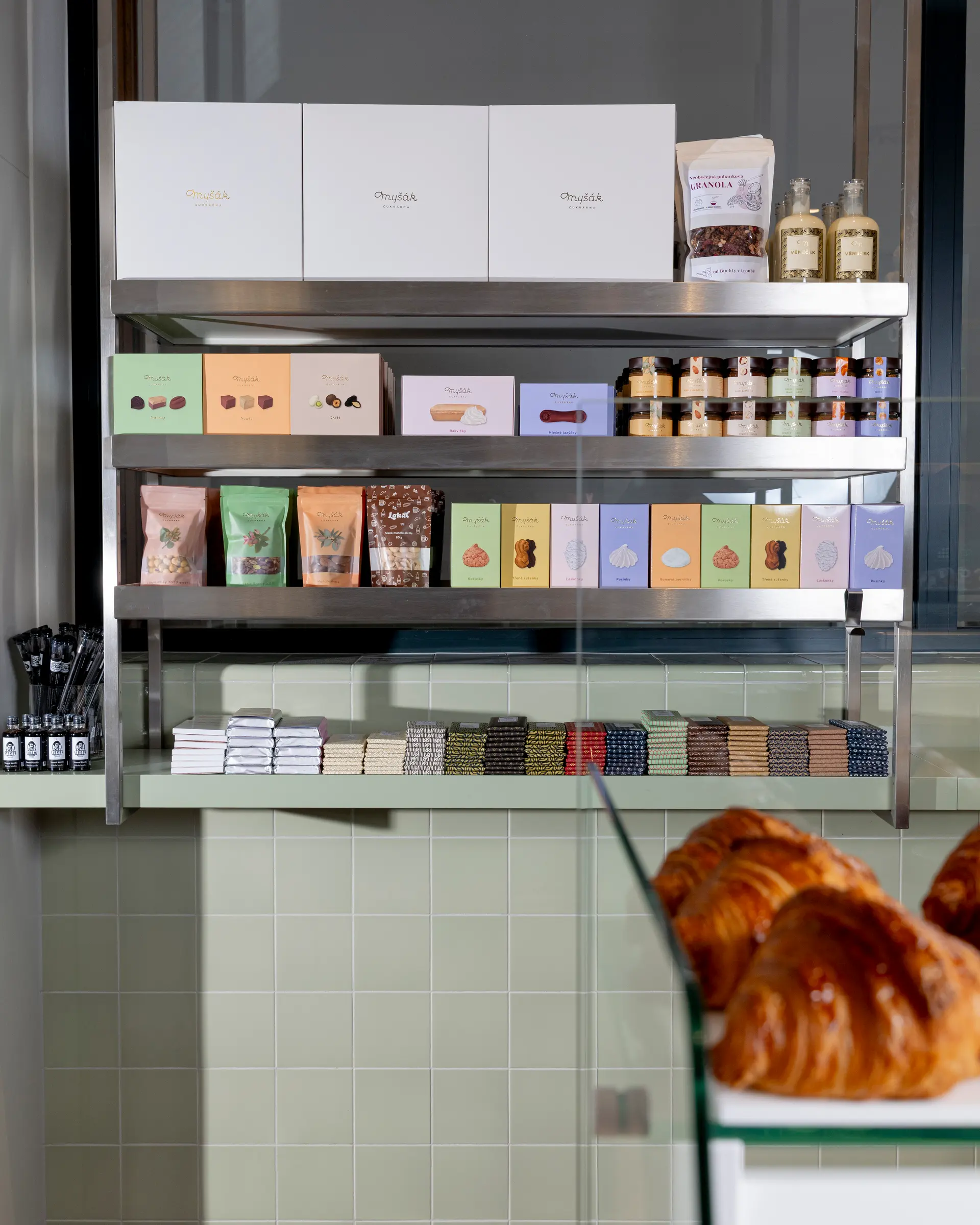 Shelf with Myšák packaged products and fresh croissants in the patisserie.