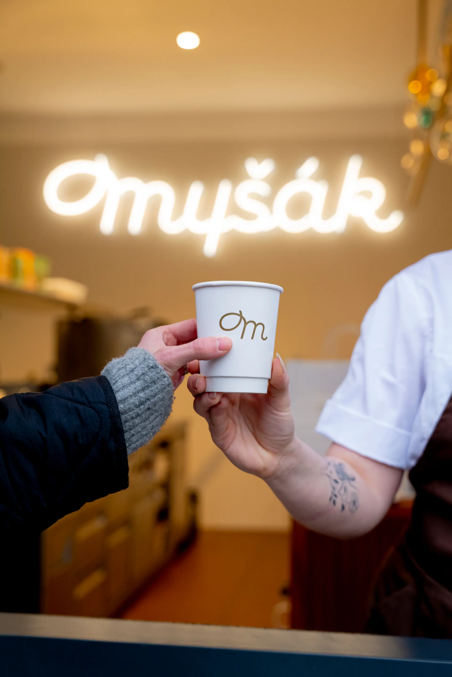 Handing over a coffee cup with Myšák logo inside the patisserie.